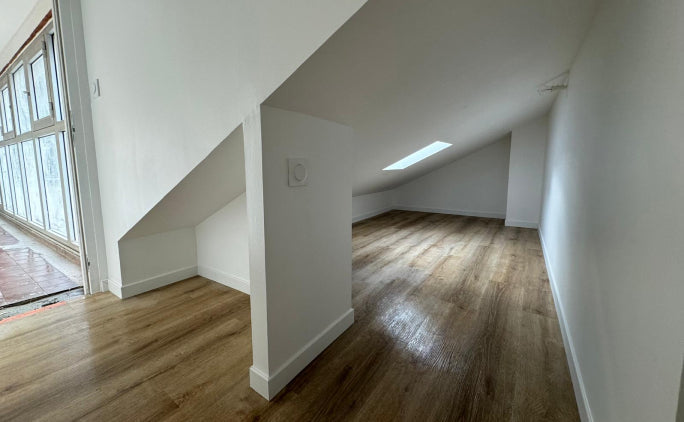 Combles aménagés avec parquet effet bois, murs blancs et isolation intérieure sous toiture rénovée