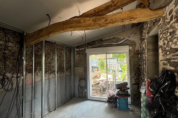 Chantier de rénovation intérieure avec ossature métallique, murs en pierre apparente et poutres en bois anciennes